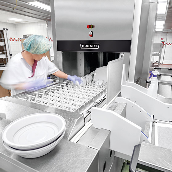 Empleado cargando platos en un lavavajillas industrial HOBART en una cocina profesional