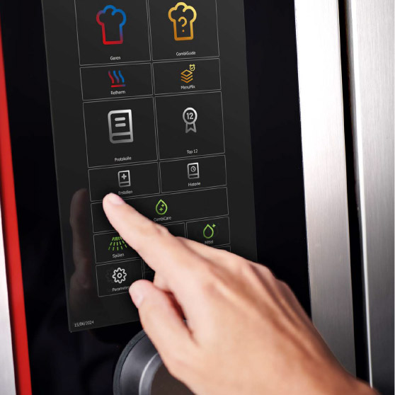 Primer plano de un dedo interactuando con un menú táctil que muestra varios iconos de funciones como Cocción, CombiGuide, Retherm, MenuPlus, Registros, Configuración y Limpieza.iGuide, Retherm, MenuPlus, Logs, Settings, and Cleaning.