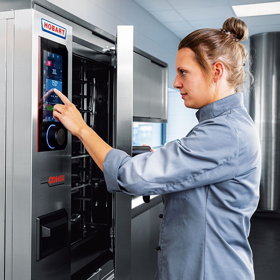 Una persona maneja la pantalla táctil de un equipo CHEF'S COMBI – con ajustes de tiempo y temperatura como “30” y “150°”, que permiten un control preciso en cocinas profesionales.