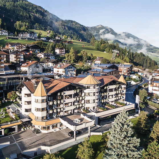 Vista aérea del Gardena Grödnerhof en Ortisei, un hotel de cinco estrellas Relais & Châteaux con más de cien años de historia, rodeado de paisajes alpinos verdes y arquitectura tradicional del valle de Gardena.