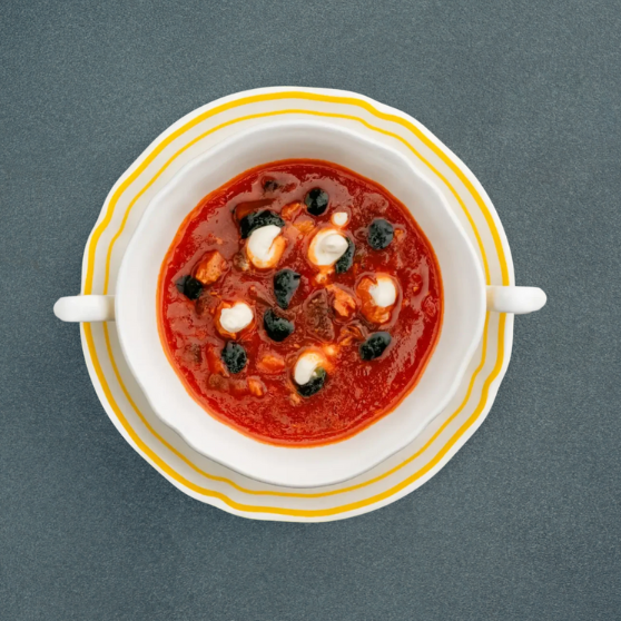 Cuenco blanco con Solyanka, una sopa tradicional de Europa del Este a base de tomate, adornada con crema agria y aceitunas negras, servida sobre plato con rayas amarillas