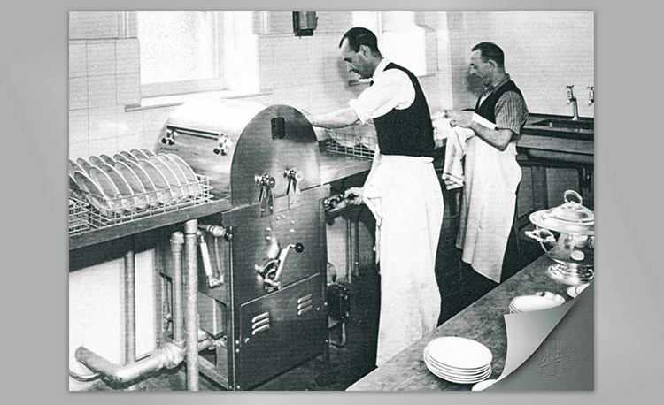 Imagen histórica de una zona de lavado comercial con gran lavavajillas Hobart y cestas de platos – tecnología temprana para limpieza eficiente en cocinas profesionales.