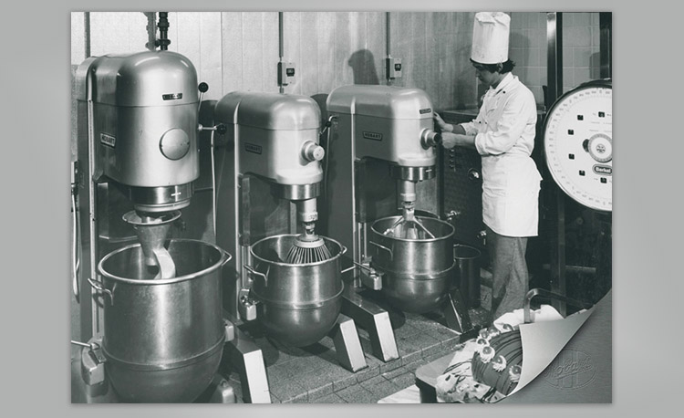 Imagen histórica de una cocina profesional con tres grandes batidoras Hobart y una báscula – tecnología temprana para mezcla eficiente y preparación de masa