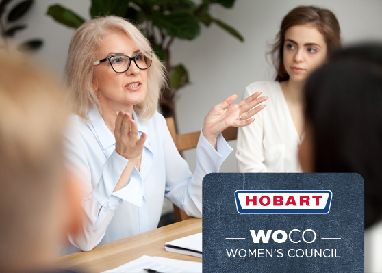 Reunión en oficina destacando el HOBART Women’s Council (WOCO), iniciativa para promover la igualdad y el desarrollo de las mujeres en la empresa. Documentos y material de escritura sobre la mesa.