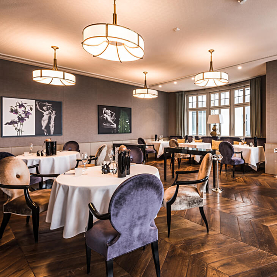 Interior elegante de un restaurante gastronómico con mesas redondas vestidas de blanco, sillas tapizadas y una iluminación cálida que crea un ambiente exclusivo.