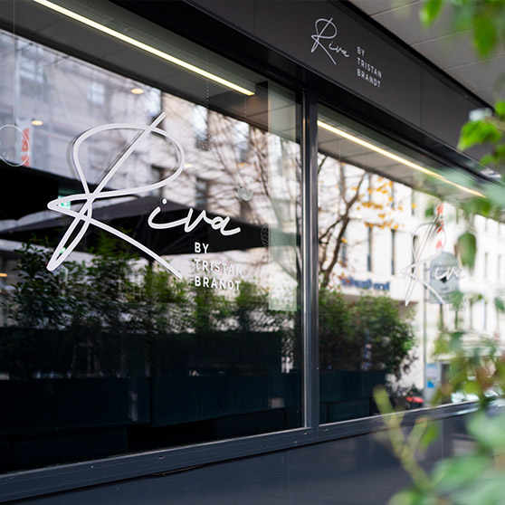 Vista exterior del restaurante RIVA by Tristan Brandt en Pforzheim con su característico logotipo en las grandes ventanas de cristal.