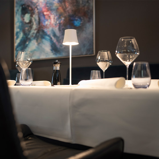 Primer plano de una mesa de alta gastronomía en el restaurante RIVA con cristalería elegante, mantelería blanca y luz moderna.