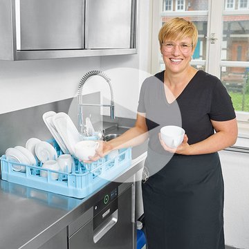 Zona de lavado moderna con superficie de acero inoxidable y lavavajillas HOBART, cesta azul con platos y cuencos limpios, persona descargando para limpieza higiénica