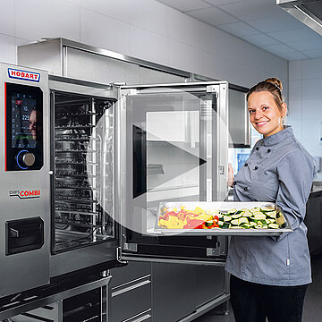 Cocina profesional con horno combinado HOBART, puerta abierta y bandeja con verduras frescas como calabacín, pimientos y zanahorias para cocción suave
